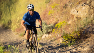 Man riding a bicycle on a rocky trail with a helmet and blue shirt.